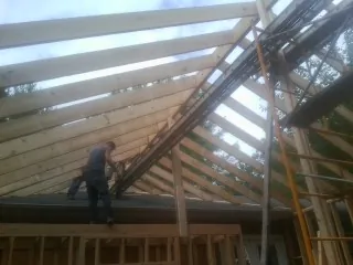Rafters going up over a new addition with a worker on the wall in De Soto